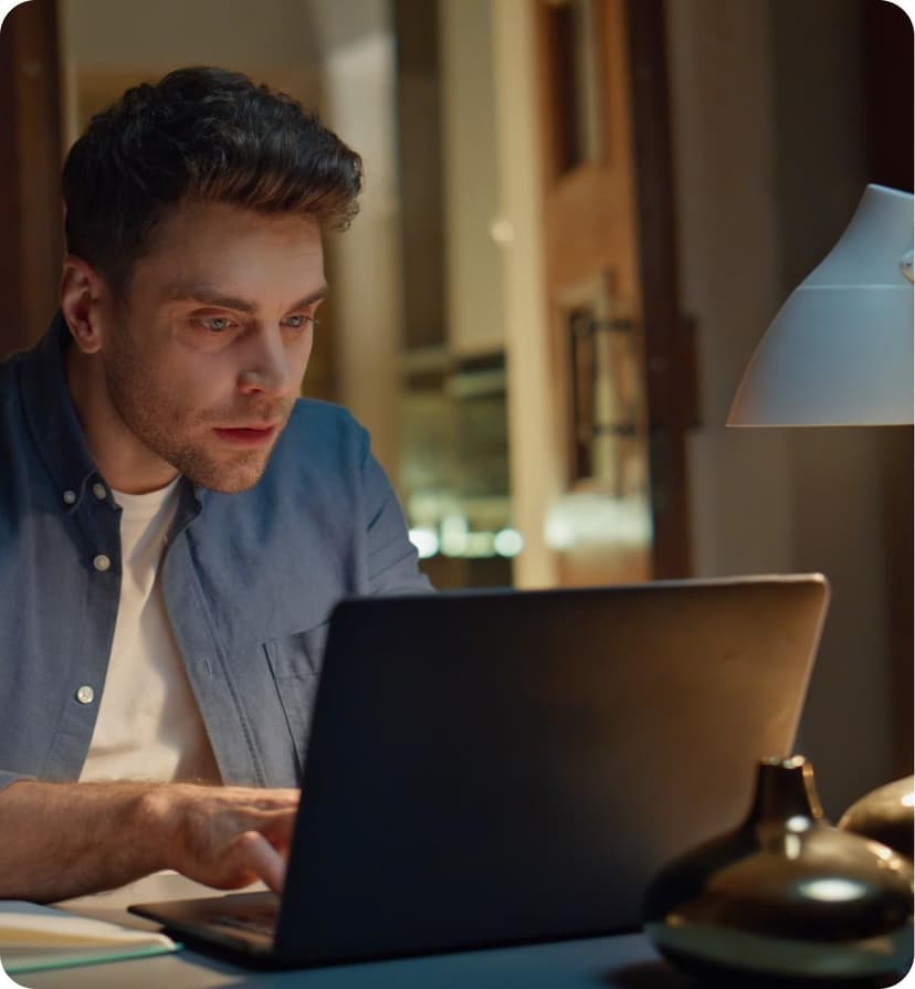 A professional man working intently on a laptop in a modern office at night.